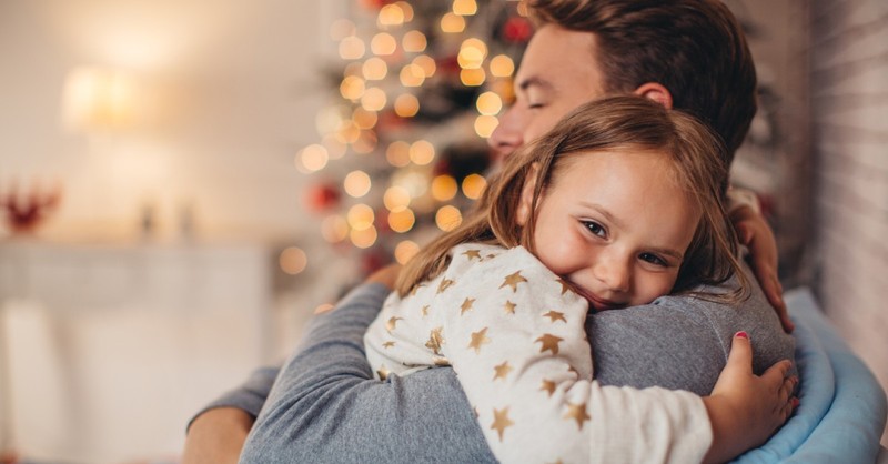 A father hugs his daughter in front of a Christmas tree