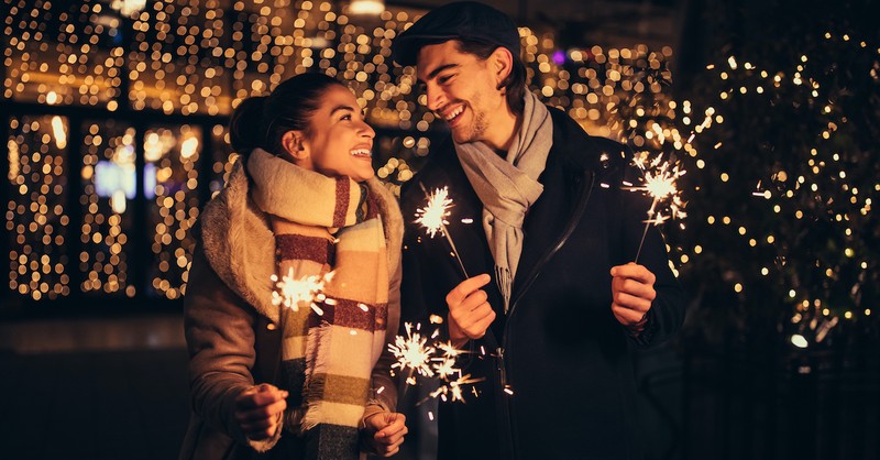 happy couple holding sparklers for New Year's bundled up for winter, marriage goals