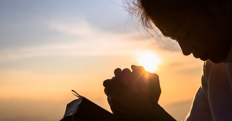 woman praying open bible sunset