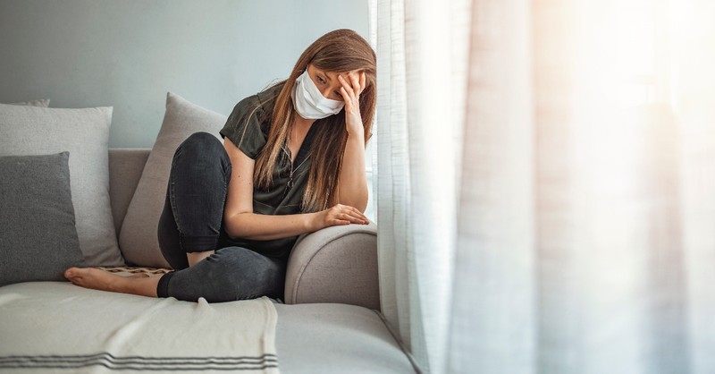 woman looking sad scared and anxious inside wearing mask alone
