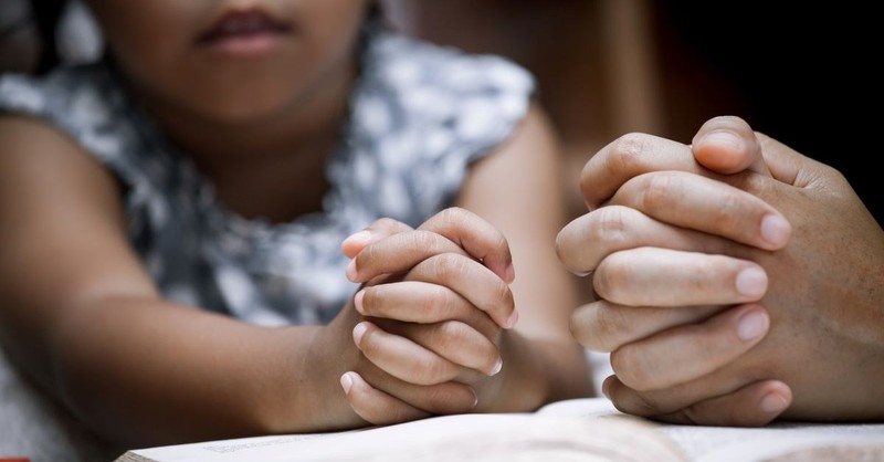 child and adult praying over bible together