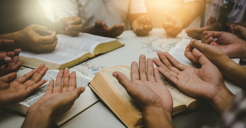 hands held over bibles, prayer for missionaries