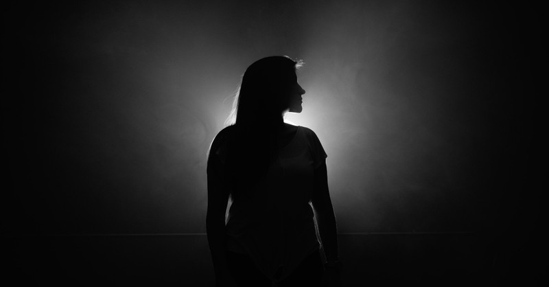 woman standing in dark in front of light