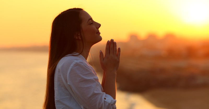 Woman praying outside under sunset, prayer for earth day