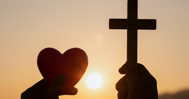 two hands holding small silhouette figures of a cross and a heart, love covers sin
