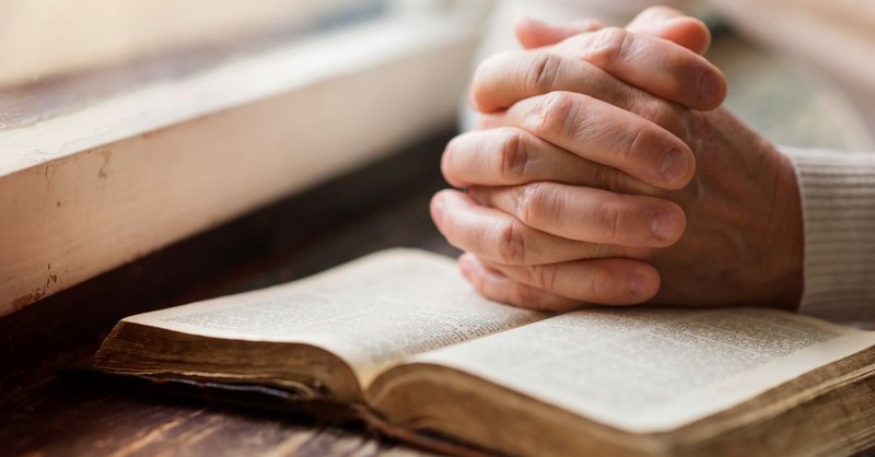 Hands folded in prayer atop an open Bible