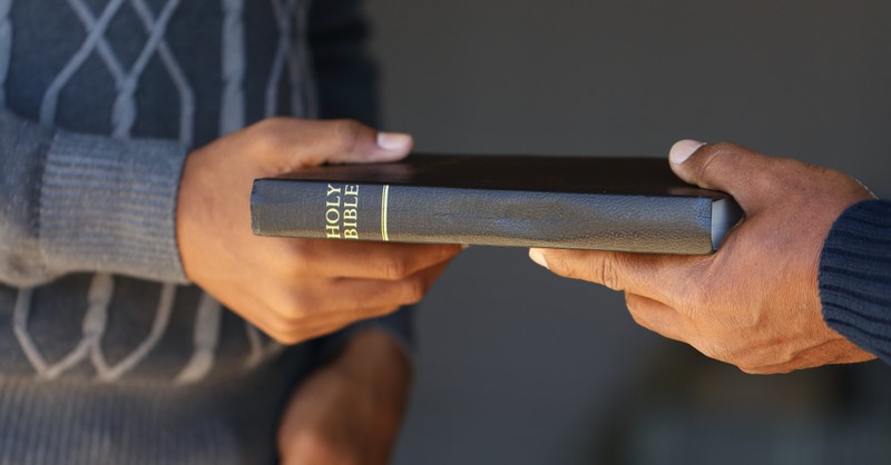 man's hand handing Bible to another man's hand