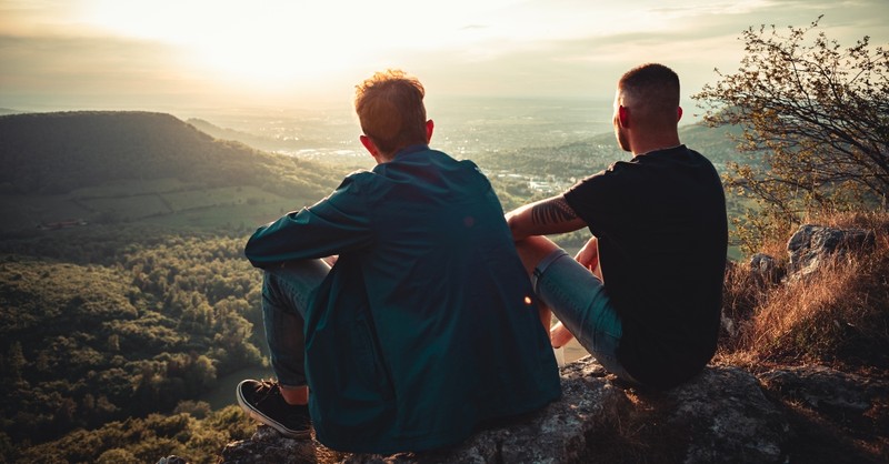 Two men sitting on a cliff looking at the sunrise