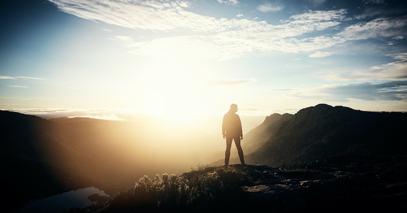 man standing on mountain side looking around at nature