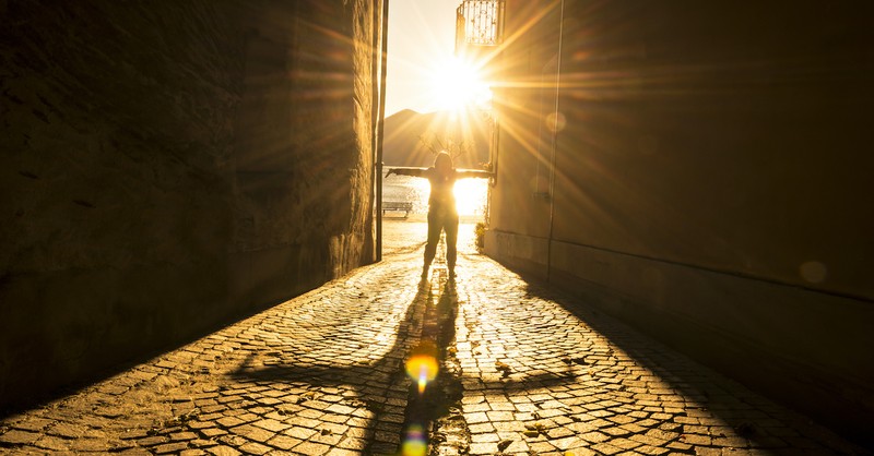 woman standing on street looking out at nature with sun reflecting on street like gold