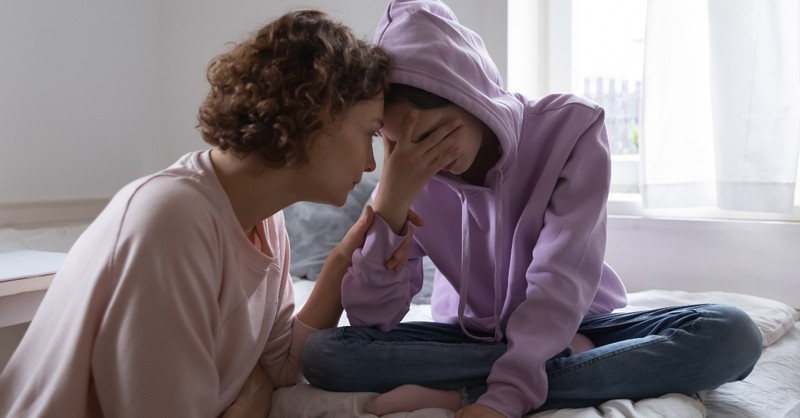 mom sitting with teen daughter who looks worried and depressed