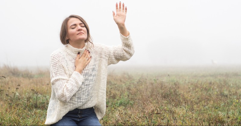 Woman kneeling in prayer with her hand up
