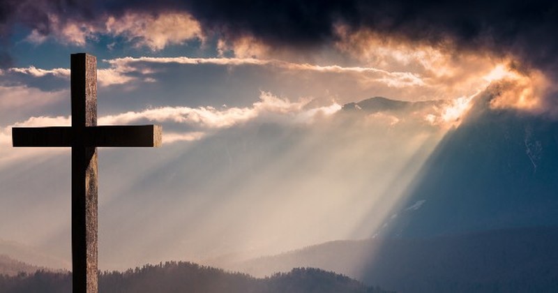 sunlight shining through clouds onto a cross on a hill, wonderful grace of jesus hymns about freedom