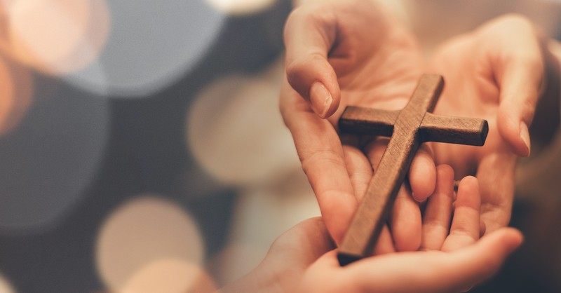 hands holding cross giving that cross to another pair of open hands