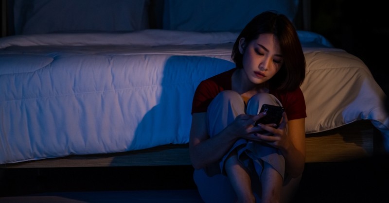 woman alone in room looking at phone in dark
