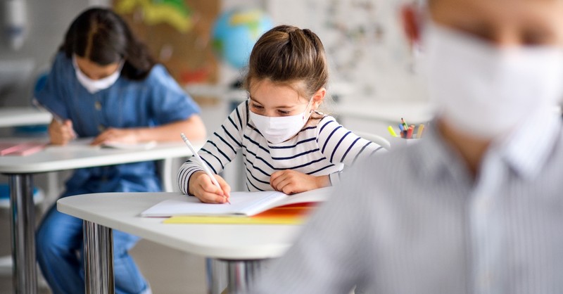 young girl student working at desk in class with mask, back to school prayers