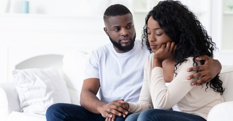 husband comforting wife who looks upset sitting on couch