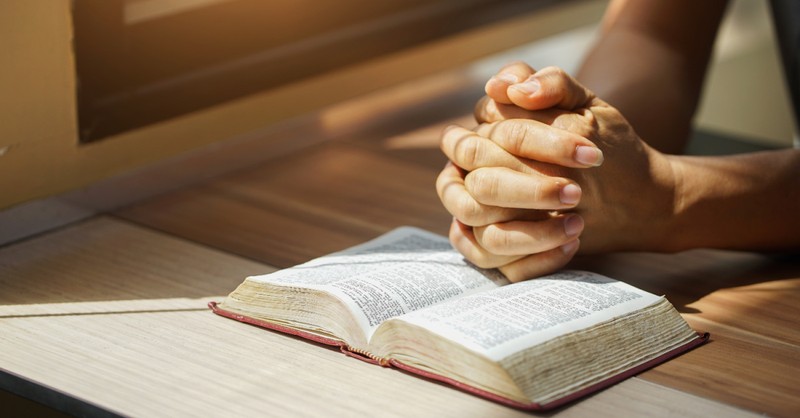 Hands folded in prayer over an open Bible