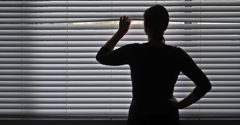 Woman fearfully looking through the widow blinds