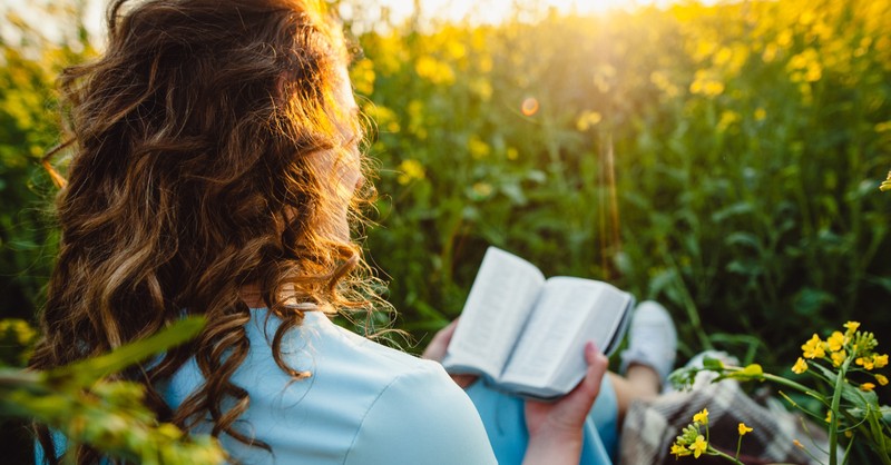 woman reading Bible in a sunlit field of flowers