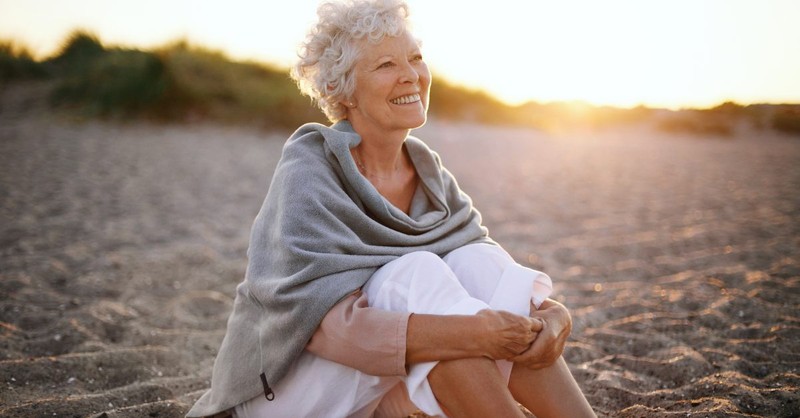 Elderly woman sitting joyfully on the beach