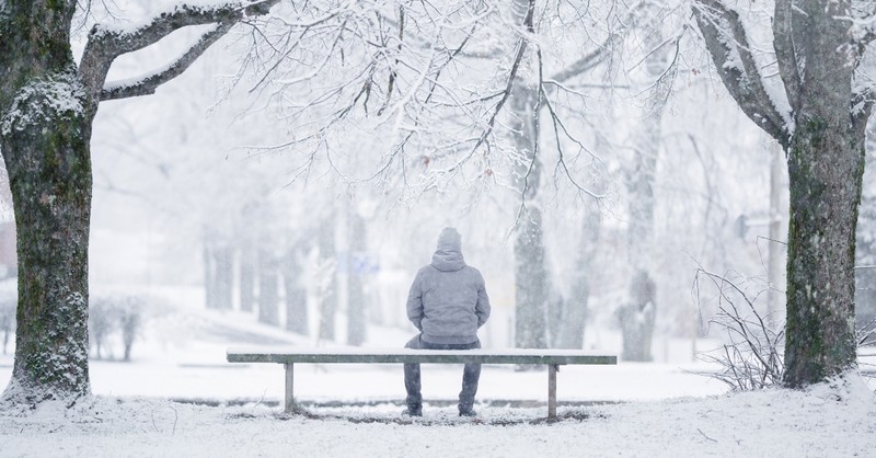 Sad man sitting alone on a bench in a snowstorm
