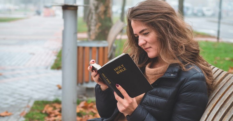 Woman reading a Bible on a park bench