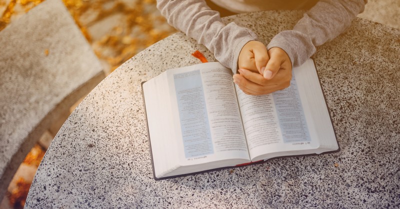 Woman with hands folded over an open Bible