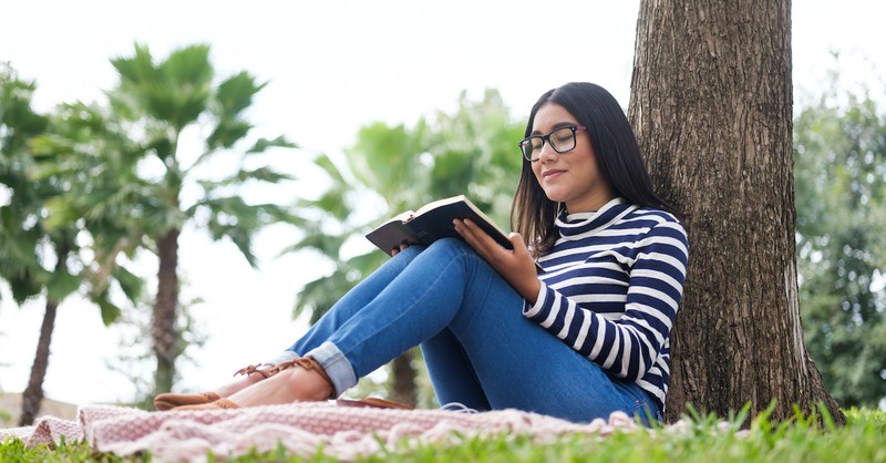 woman reading Bible in the grass against a tree, Christian values