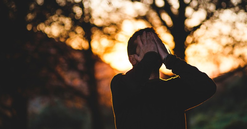 A stressed man covering his face, people who are uncertain about their faith are more likely to experience mental distress