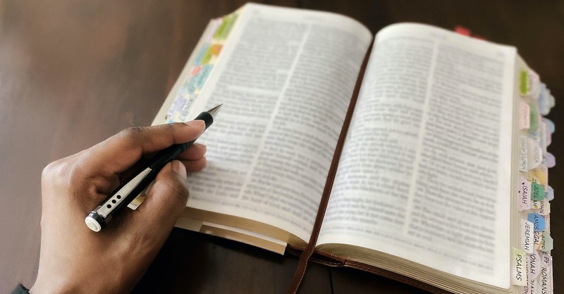 man's hand holding pen with open Bible