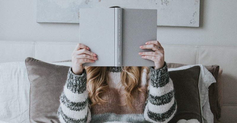 woman reading book in front of face hiding face