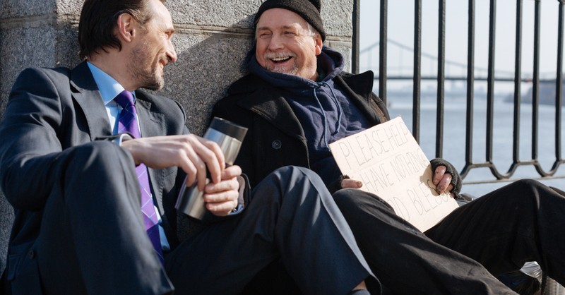 man in suit laughing and sitting with a homeless man