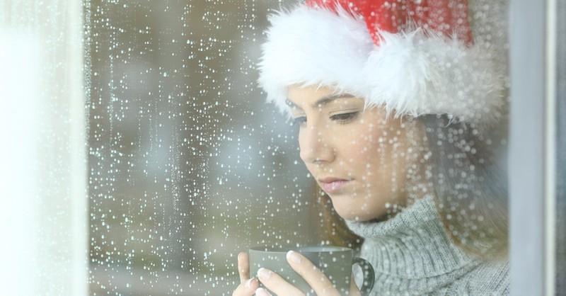 sad woman wearing a Santa hat, standing in front of a window covered in rain 