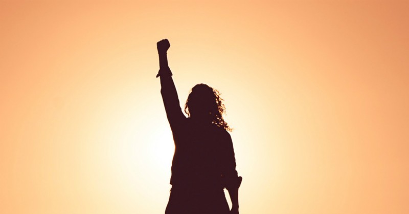 girl throwing a victorious fist in the air, facing the sun