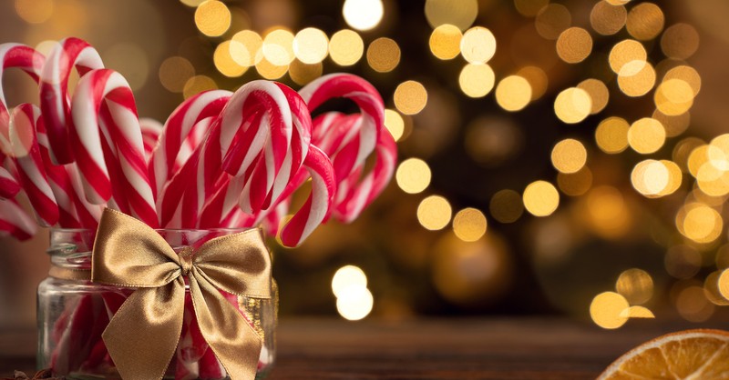 Bunch of candy canes in a jar with Christmas lights behind