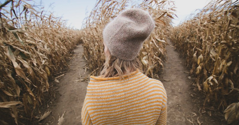 young woman standing at crossroad in a cornfield, trying to make a decision