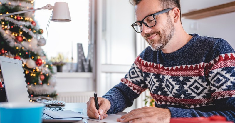 man in Christmas sweater writing a card