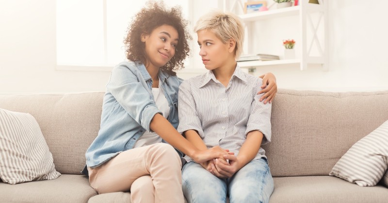 happy friend listening to upset friend sitting on couch