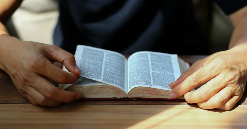 Person sitting in front of an open Bible, turning pages