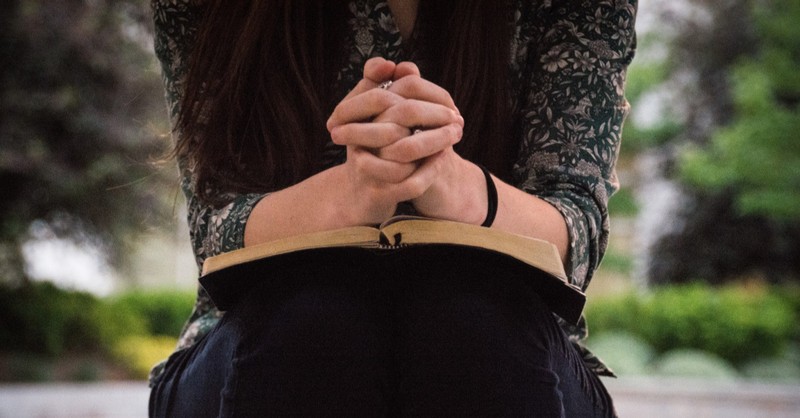 woman praying with hands folded on her Bible