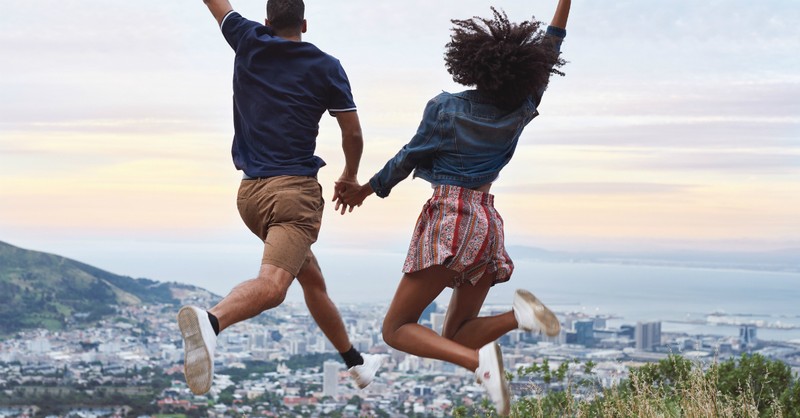 couple holding hands leaping in front of panoramic view of city