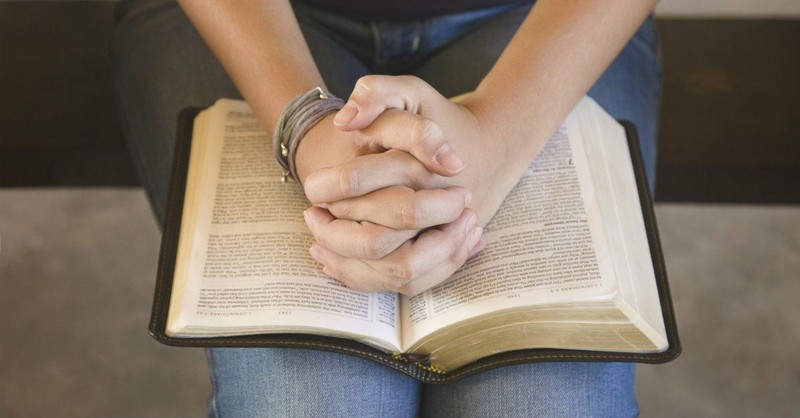 Woman with hands folded in prayer over an open Bible