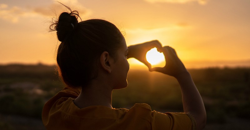 Woman making a heart symbol over the sun