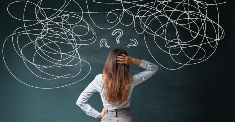 back view of woman facing chalkboard with question and swirly marks of confusion