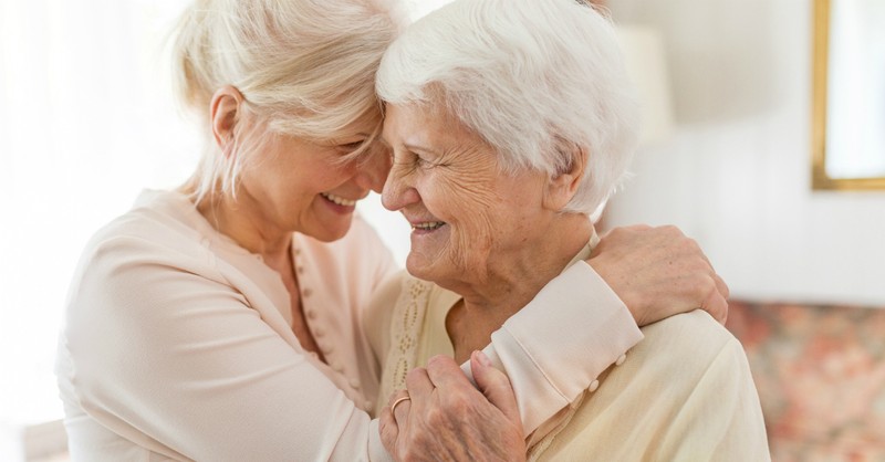 adult daughter joyful hugging senior mom with alzheimers or dementia