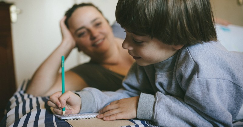 mom looking at her boy doing homework looking happy