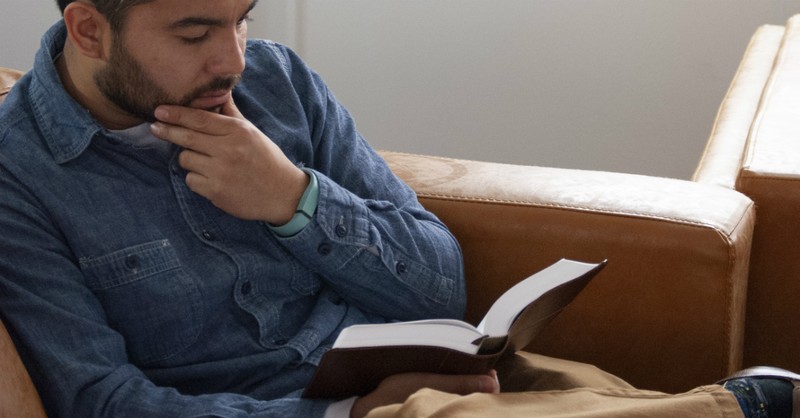 man sitting and reading bible looking thoughtful