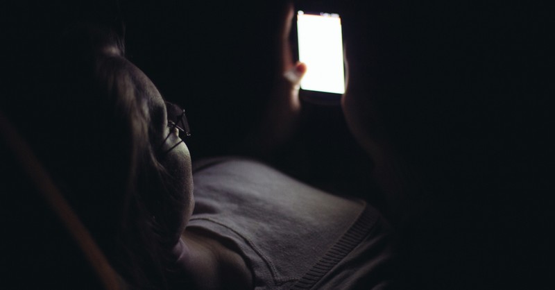 Girl laying in the dark on her phone, bright light