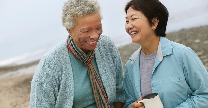 two senior women laughing together on the beach